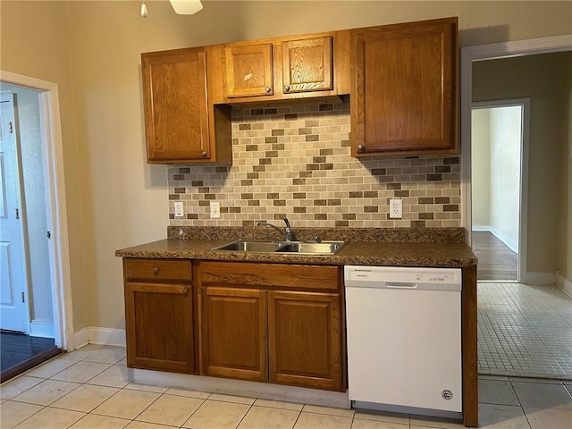 kitchen with dark countertops, brown cabinets, white dishwasher, and a sink