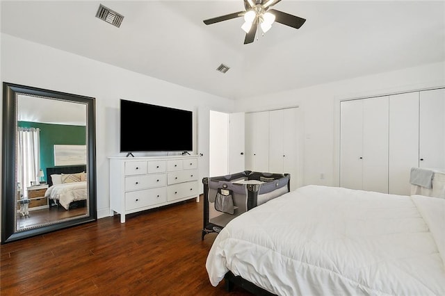 bedroom with ceiling fan, dark wood-type flooring, and two closets