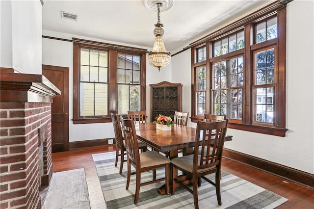 dining area with a notable chandelier, dark hardwood / wood-style floors, a fireplace, and a wealth of natural light