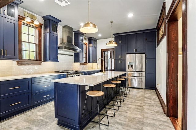 kitchen with a kitchen breakfast bar, stainless steel appliances, wall chimney range hood, hanging light fixtures, and an island with sink