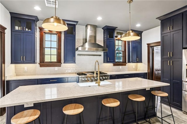 kitchen featuring a kitchen island with sink, decorative light fixtures, wall chimney range hood, and blue cabinets