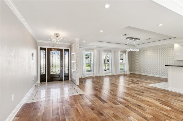 entryway featuring light hardwood / wood-style floors, a raised ceiling, ornamental molding, and a chandelier