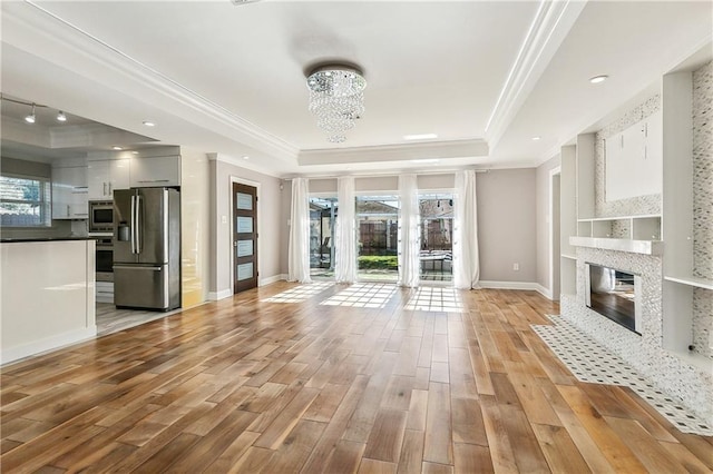 unfurnished living room featuring a raised ceiling, light hardwood / wood-style flooring, plenty of natural light, and ornamental molding