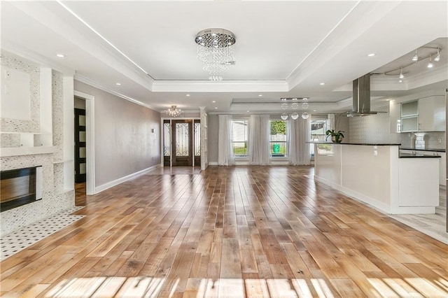 unfurnished living room featuring a notable chandelier, a raised ceiling, and light wood-type flooring