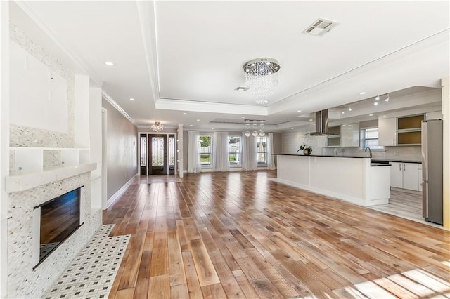 unfurnished living room featuring an inviting chandelier, ornamental molding, a tray ceiling, and light hardwood / wood-style flooring