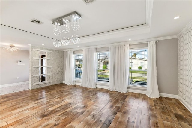 unfurnished living room featuring a wealth of natural light, hardwood / wood-style floors, ornamental molding, and an inviting chandelier