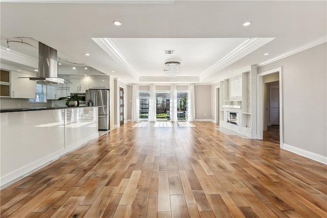 unfurnished living room with a chandelier, light hardwood / wood-style floors, ornamental molding, and a tray ceiling