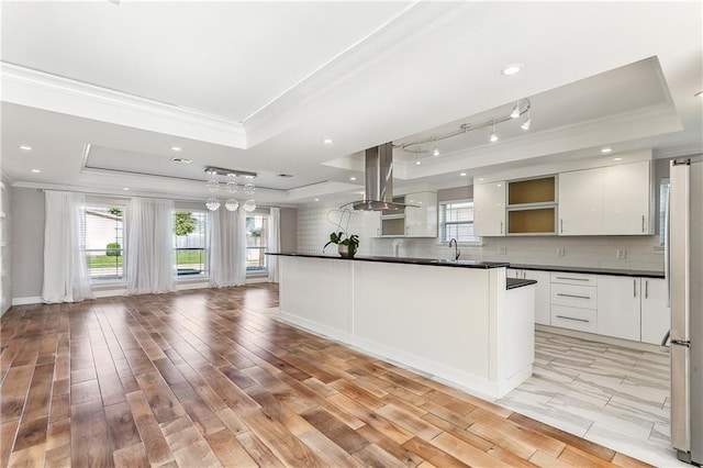 kitchen featuring a tray ceiling, island range hood, white cabinets, and light hardwood / wood-style floors