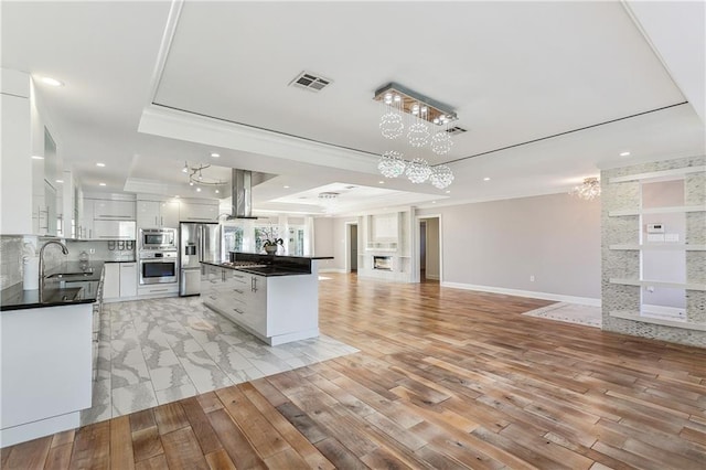 kitchen with stainless steel appliances, a raised ceiling, island range hood, white cabinets, and light wood-type flooring