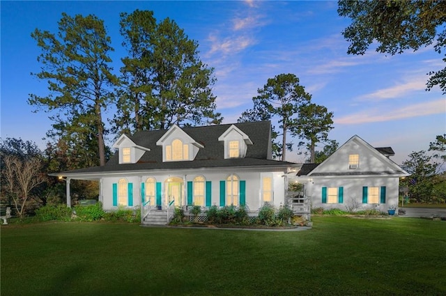 back house at dusk featuring a lawn and a porch