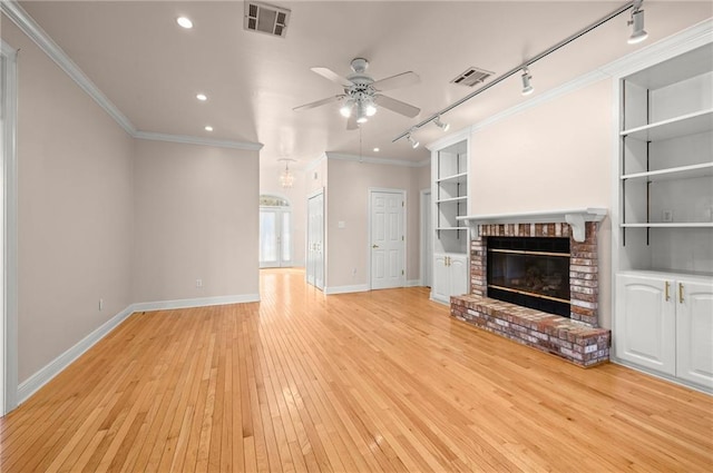 unfurnished living room featuring rail lighting, a brick fireplace, ornamental molding, ceiling fan, and light hardwood / wood-style floors