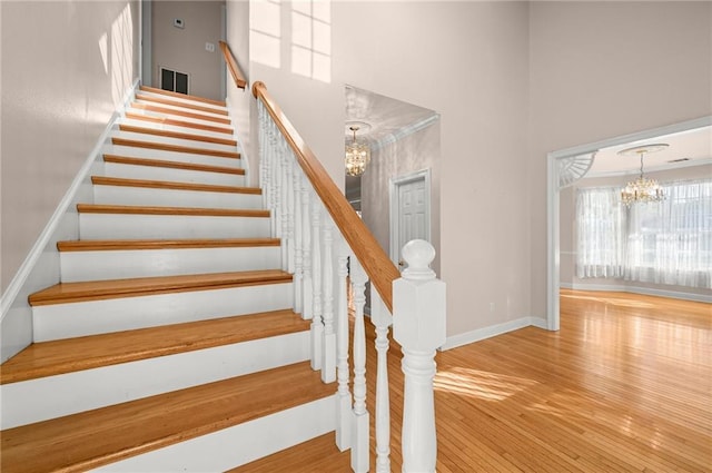 staircase featuring a chandelier, wood-type flooring, ornamental molding, and a high ceiling