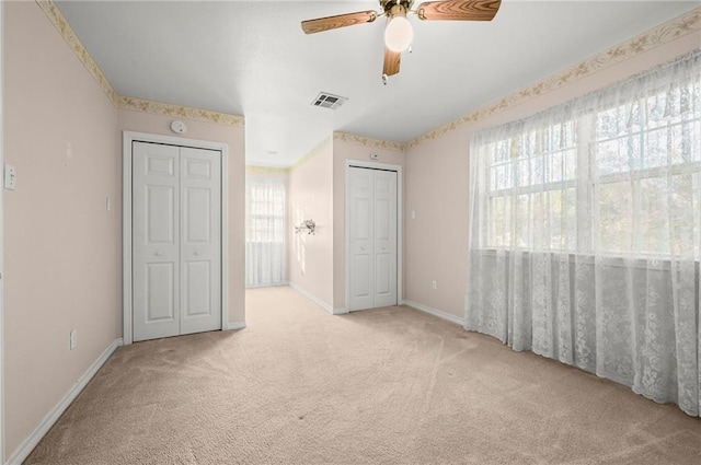 unfurnished bedroom with ceiling fan, light colored carpet, and multiple closets