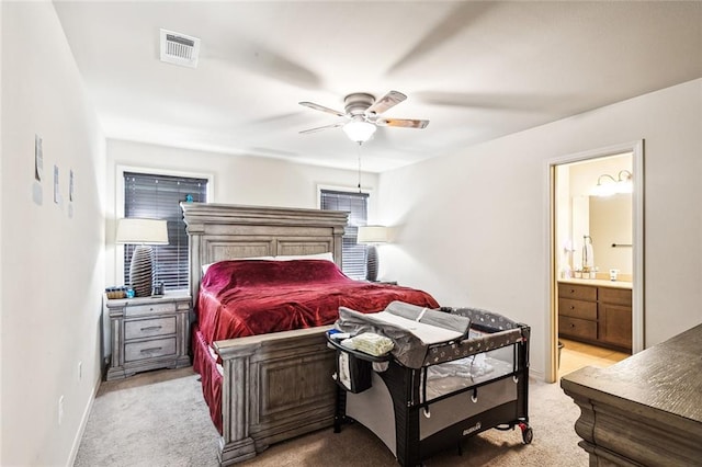 bedroom featuring light carpet, ensuite bathroom, and ceiling fan