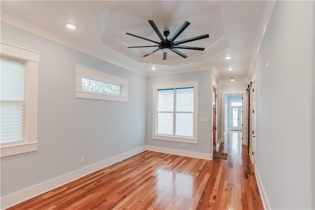 unfurnished room with a barn door, crown molding, ceiling fan, and light hardwood / wood-style floors