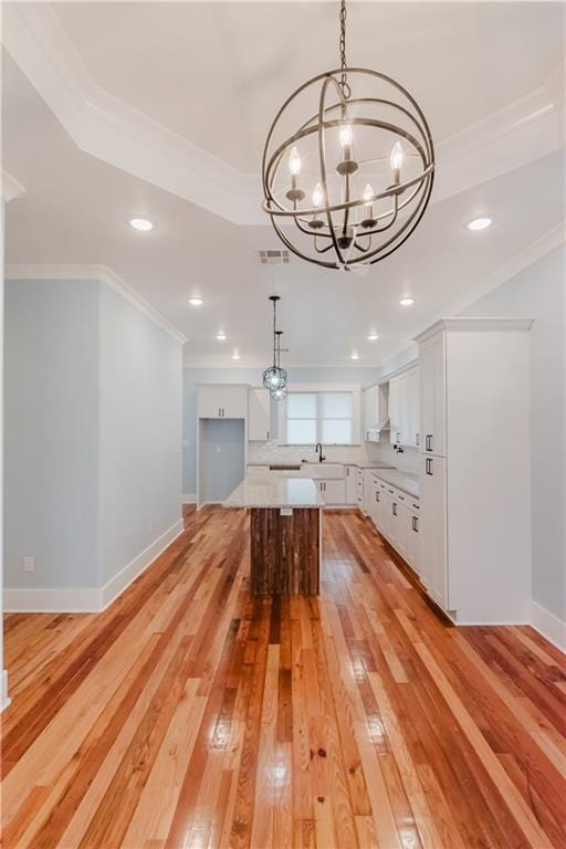 kitchen featuring white cabinetry, wall chimney range hood, light hardwood / wood-style floors, decorative light fixtures, and a kitchen island