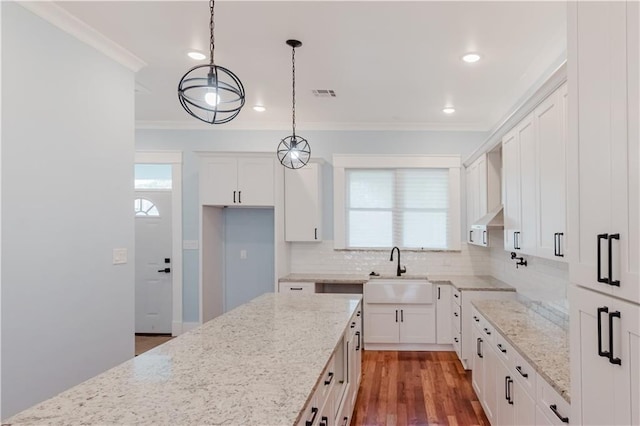 kitchen with light stone counters, decorative light fixtures, white cabinetry, and sink