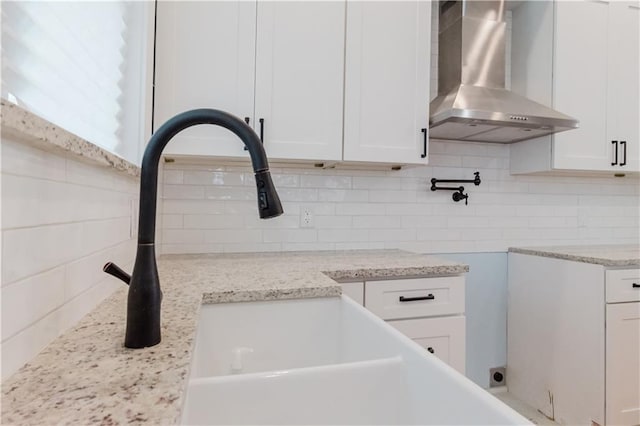 details featuring backsplash, white cabinetry, light stone countertops, and wall chimney range hood