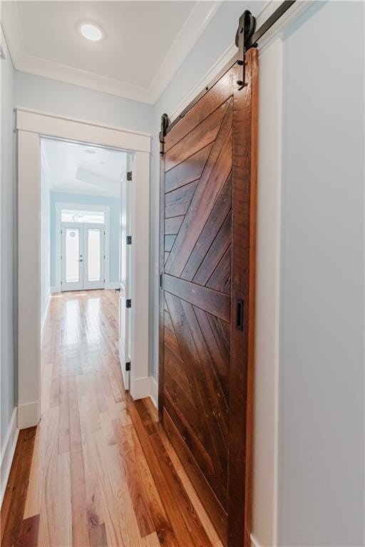 hallway with a barn door, crown molding, light hardwood / wood-style flooring, and french doors