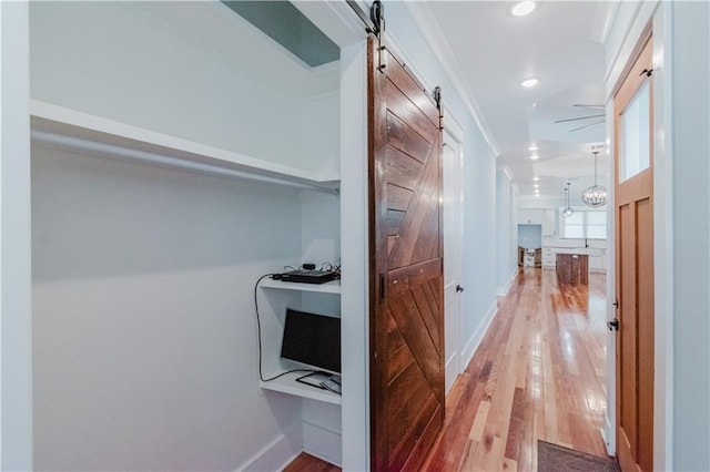 hallway featuring light wood-type flooring, a barn door, and ornamental molding