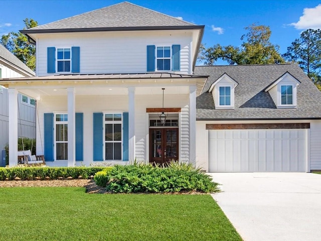 view of front of property featuring an attached garage, a standing seam roof, a porch, roof with shingles, and a front yard