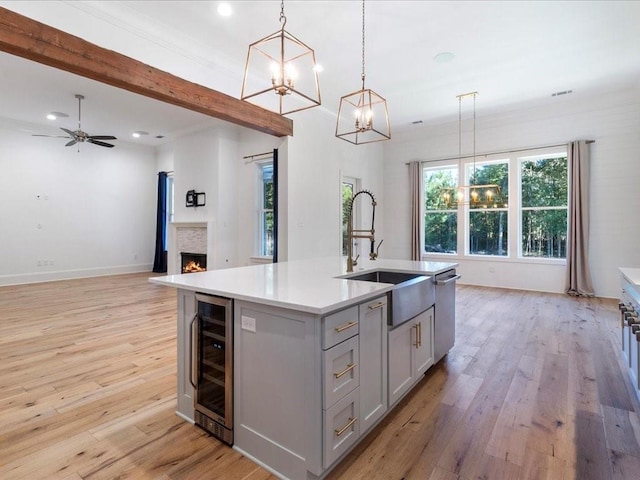 kitchen featuring sink, hanging light fixtures, beverage cooler, a center island with sink, and light wood-type flooring