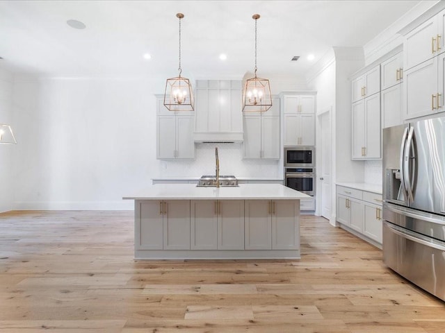 kitchen featuring a center island with sink, hanging light fixtures, light wood-type flooring, and appliances with stainless steel finishes