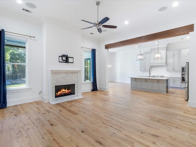 unfurnished living room with sink, ceiling fan, ornamental molding, a fireplace, and light hardwood / wood-style floors