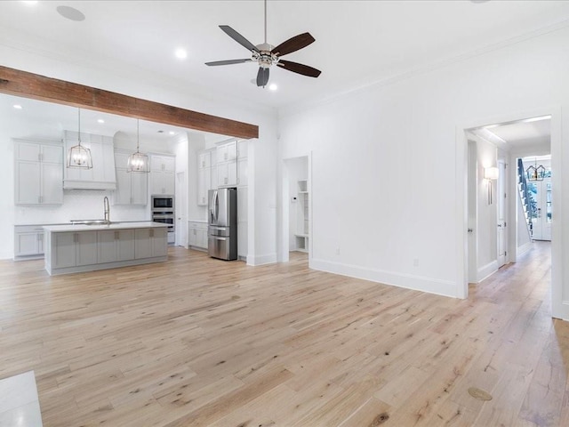 unfurnished living room with light wood finished floors, baseboards, a ceiling fan, crown molding, and a sink