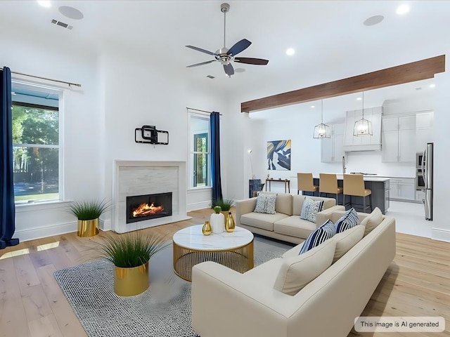 living room with a warm lit fireplace, plenty of natural light, visible vents, and a ceiling fan
