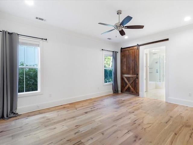 unfurnished room featuring a barn door, light hardwood / wood-style flooring, ceiling fan, and crown molding