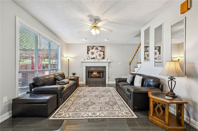 living room featuring a textured ceiling, ceiling fan, and a tiled fireplace