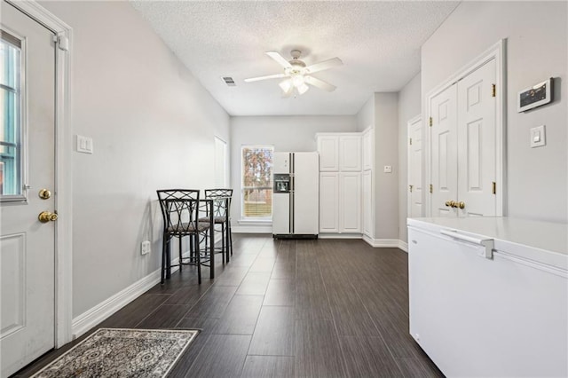 kitchen with a textured ceiling, white cabinetry, dark wood-type flooring, and white refrigerator with ice dispenser