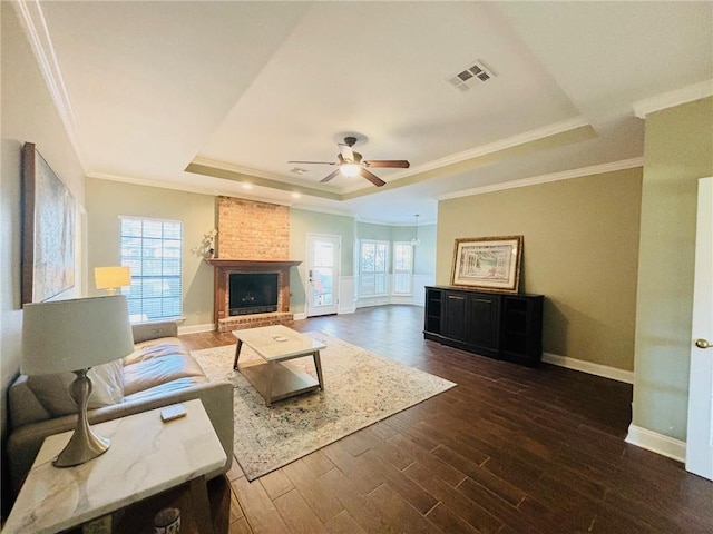 living room featuring a tray ceiling, a brick fireplace, dark hardwood / wood-style flooring, and ornamental molding