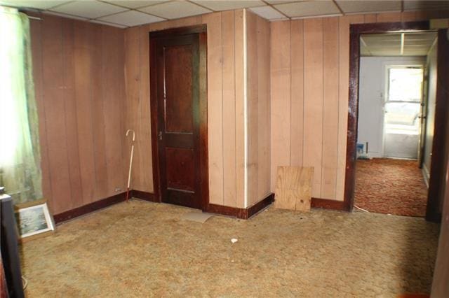 spare room with carpet flooring, a paneled ceiling, and wood walls