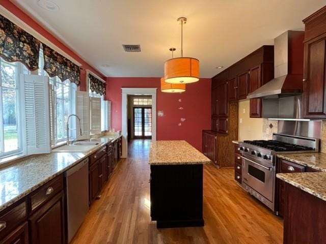 kitchen with pendant lighting, a center island, light hardwood / wood-style flooring, wall chimney exhaust hood, and stainless steel appliances