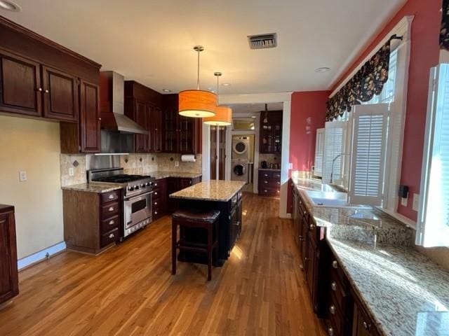 kitchen with a center island, wall chimney exhaust hood, hanging light fixtures, stacked washer / dryer, and high end stainless steel range