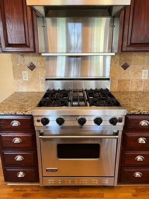 kitchen with tasteful backsplash, light stone countertops, designer range, and wood-type flooring