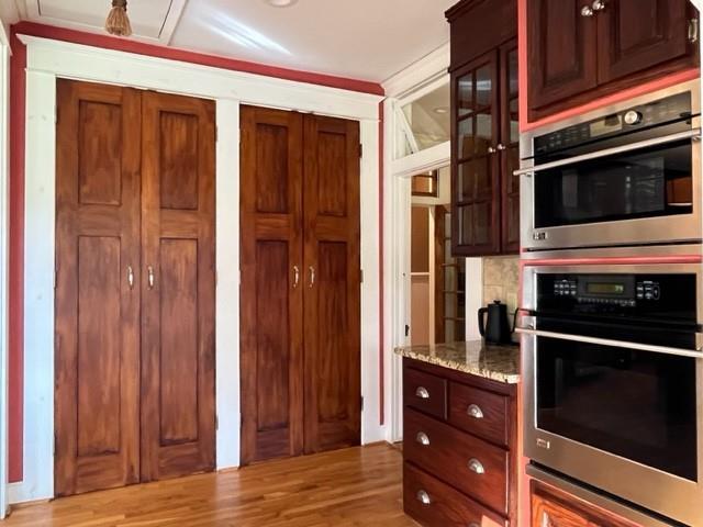 kitchen with light stone counters, stainless steel double oven, and light hardwood / wood-style floors