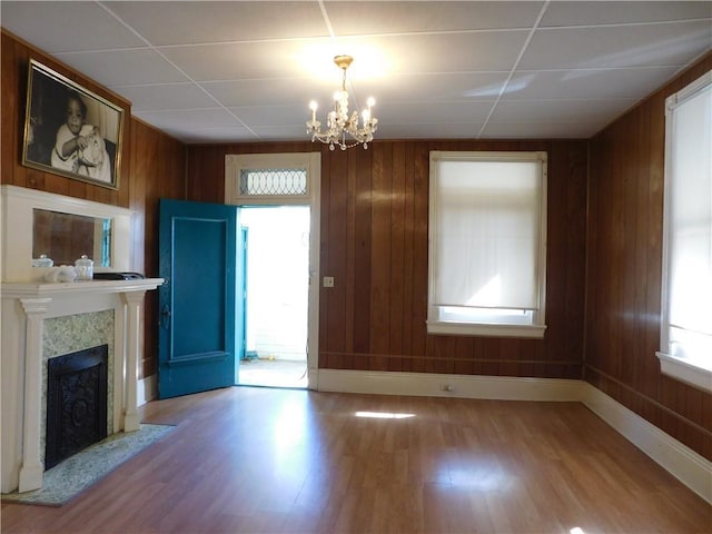 unfurnished living room featuring a fireplace, wood-type flooring, wooden walls, and a notable chandelier