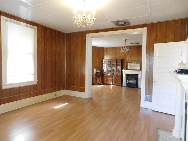 unfurnished living room featuring hardwood / wood-style floors, a notable chandelier, and wooden walls