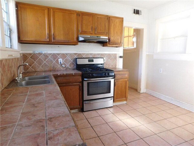 kitchen with decorative backsplash, gas range, sink, tile countertops, and light tile patterned flooring