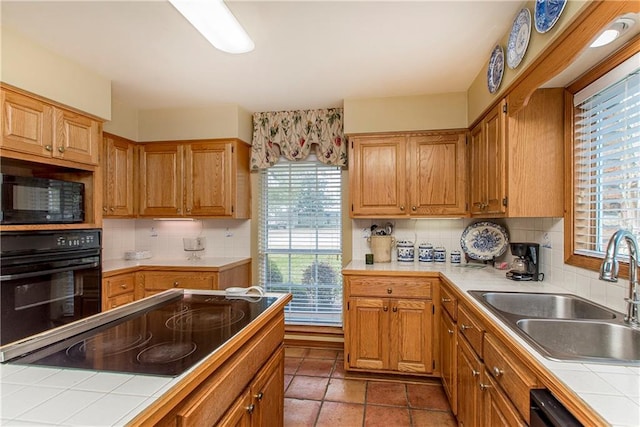 kitchen with sink, tile countertops, backsplash, and black appliances