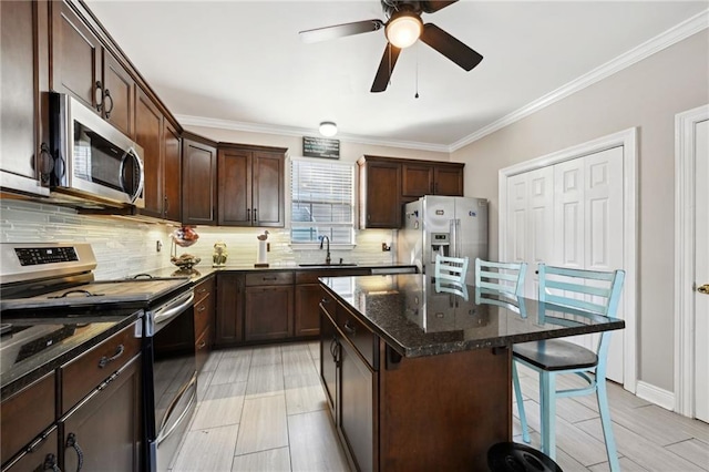 kitchen with appliances with stainless steel finishes, ornamental molding, dark stone counters, sink, and a kitchen island