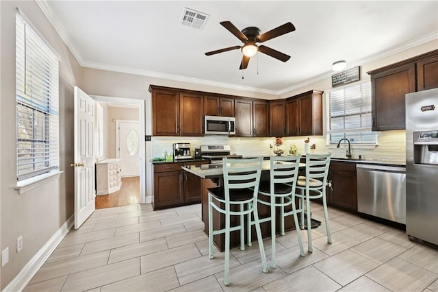 kitchen with decorative backsplash, a kitchen bar, dark brown cabinetry, stainless steel appliances, and a center island