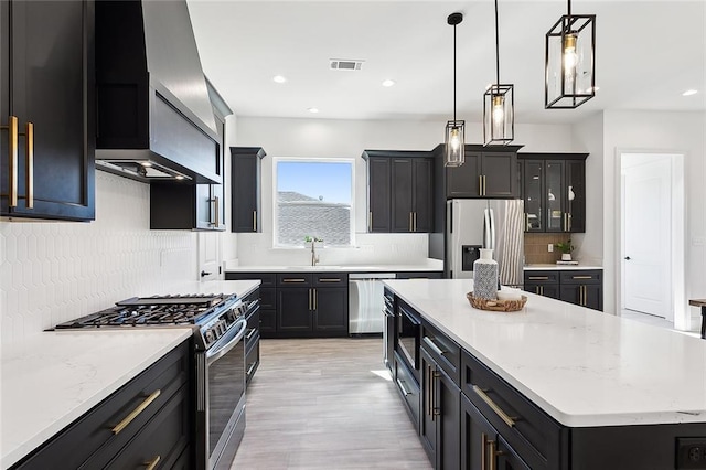 kitchen with appliances with stainless steel finishes, backsplash, wall chimney range hood, pendant lighting, and a kitchen island