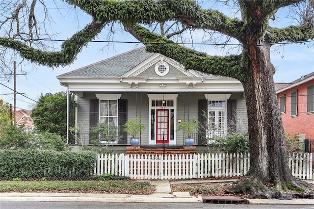 view of front of home with a fenced front yard, a porch, and roof with shingles