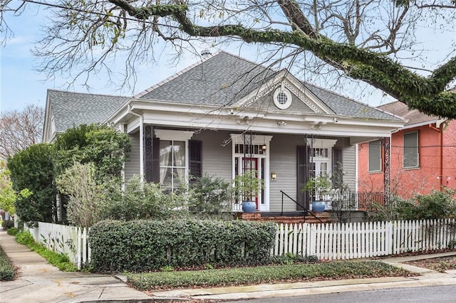 view of front of property with a shingled roof, a fenced front yard, and a porch