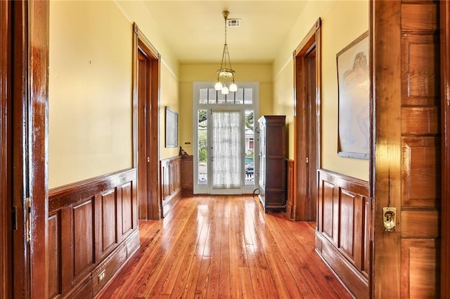 doorway with a wainscoted wall, a notable chandelier, visible vents, and light wood finished floors