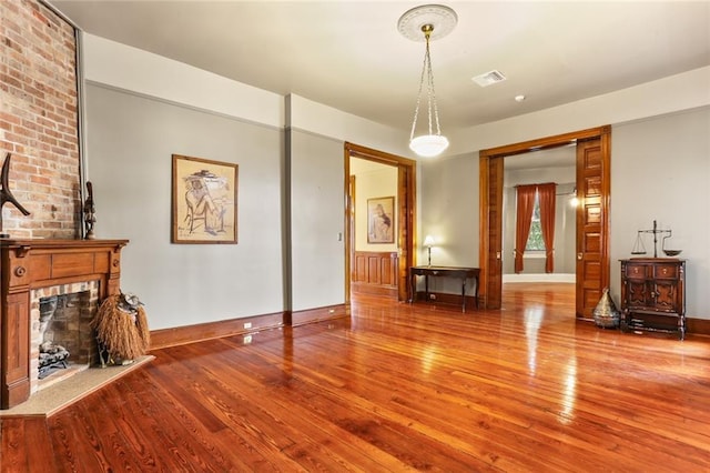 unfurnished living room with a large fireplace, visible vents, baseboards, and wood finished floors